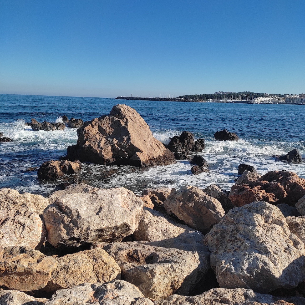 Rocky shoreline with ocean waves, blue sky, and distant coast