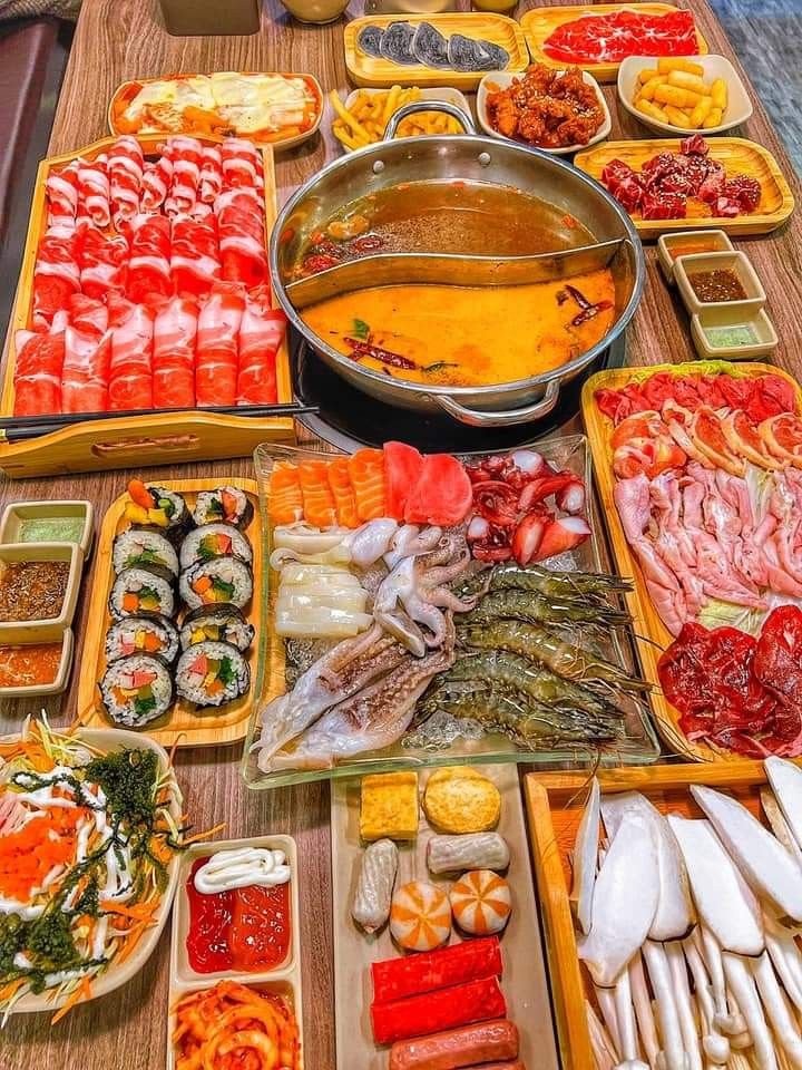 Hot pot dining setup with colorful ingredients spread around a central cooking pot on a wooden table