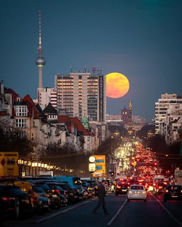 Full moon rising over Berlin cityscape with TV Tower and busy street traffic at dusk
