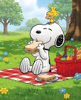 Snoopy sitting on picnic blanket with Woodstock perched on his head, red basket beside them in grassy field