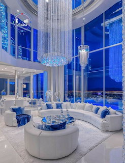 Luxurious white lounge with curved sofas, crystal chandeliers, and tall blue windows
