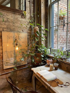 Cozy café corner with wooden table, climbing plants, brick walls, and a vintage New Orleans map by large windows