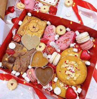 Red gift box filled with heart-shaped cookies, macarons, and candies in pink, brown, and gold colors for Valentine's Day