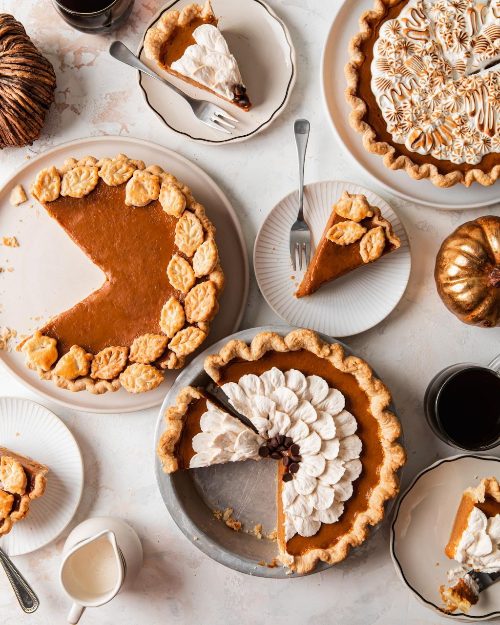 Overhead view of several fall pies with decorative crusts on white marble table with coffee and small pumpkins