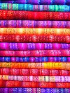 Stack of brightly colored woven fabrics in pink, purple, red, blue, green, and orange hues