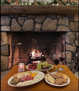Stone fireplace with fire burning behind a table with charcuterie, cheese, fruit, crackers and red wine