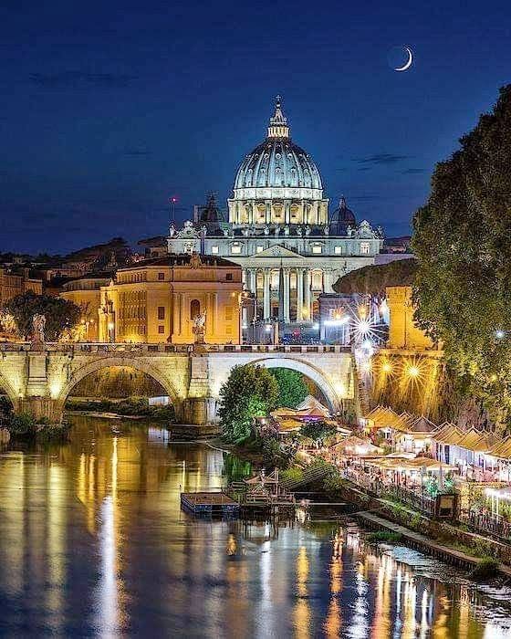 St Peter's Basilica at night above a bridge and river reflections in Rome
