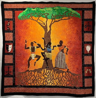 Colorful textile art showing silhouetted figures around a tree with orange sky and patterned border
