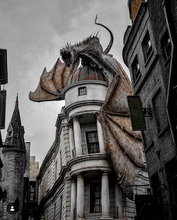 Large dragon sculpture perched on top of a white domed building in a themed wizarding area