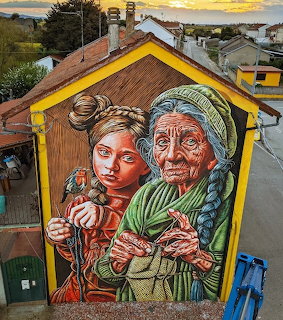 Colorful street art mural of a young girl and elderly woman on a house wall in a village
