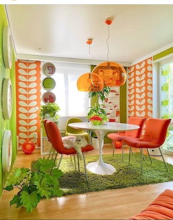 Colorful 1970s retro dining room with orange chairs, white tulip table, patterned curtains, and green rug