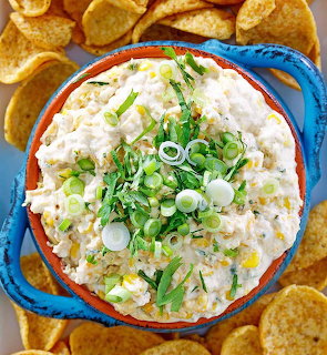 Creamy street corn dip with green onion garnish in a blue dish surrounded by tortilla chips.