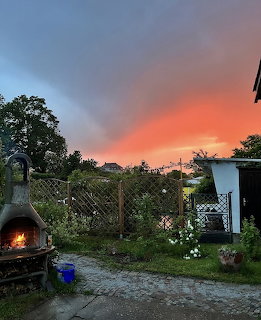Dramatic orange sunset sky over garden with trees and outdoor pizza oven