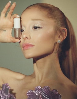 Portrait of Ariana Grande holding makeup product in purple feathered outfit