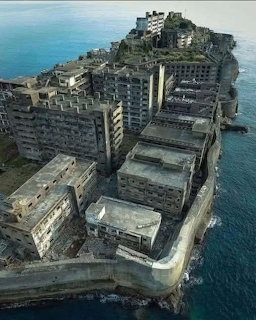 Aerial photo of abandoned Gunkanjima Island with decaying concrete buildings surrounded by dark ocean