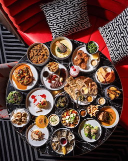 Overhead flatlay of colorful brunch dishes with eggs, bread, salads, and various foods on a red table