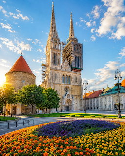 Zagreb Cathedral twin spires behind vibrant orange and yellow flower beds at sunset