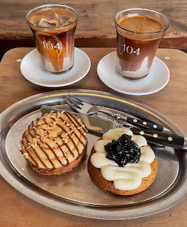 Two coffees in glass cups and two decorated pastry tarts on a silver tray on a wooden table