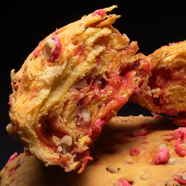 Close-up of a flaky golden pastry with pink praline pieces on a black background