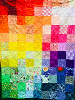 Rainbow gradient patchwork quilt with squares in red, yellow, green, blue, and purple fabrics with various patterns
