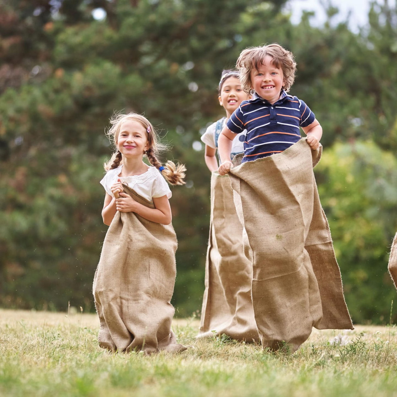 Three children doing a sack race on grass outdoors