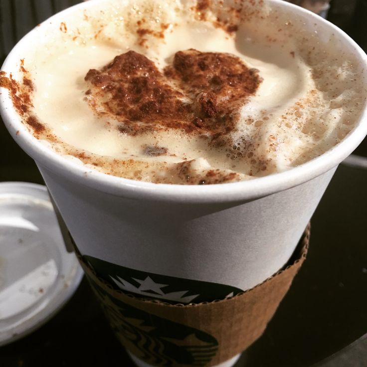 Cappuccino with heart-shaped cinnamon latte art in white disposable cup with brown cardboard sleeve