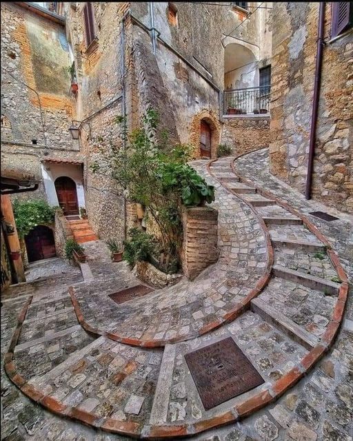 Curved coblestone staircase in a medieval Italian village with stone walls and greenery