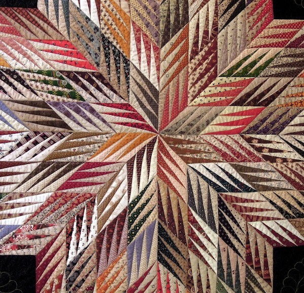Colorful star quilt with radiating geometric pattern in striped fabrics on black