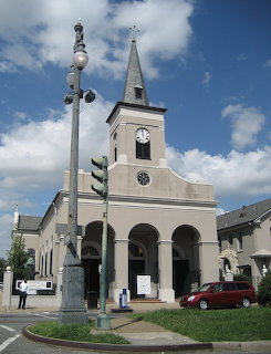 Church exterior with steeple, arched entrance, streetlight, and red car under a blue sky