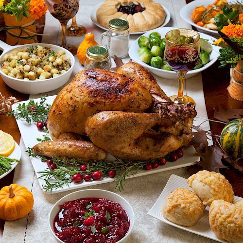 Thanksgiving dinner table with roasted turkey, cranberry sauce, side dishes, pumpkins and fall flowers
