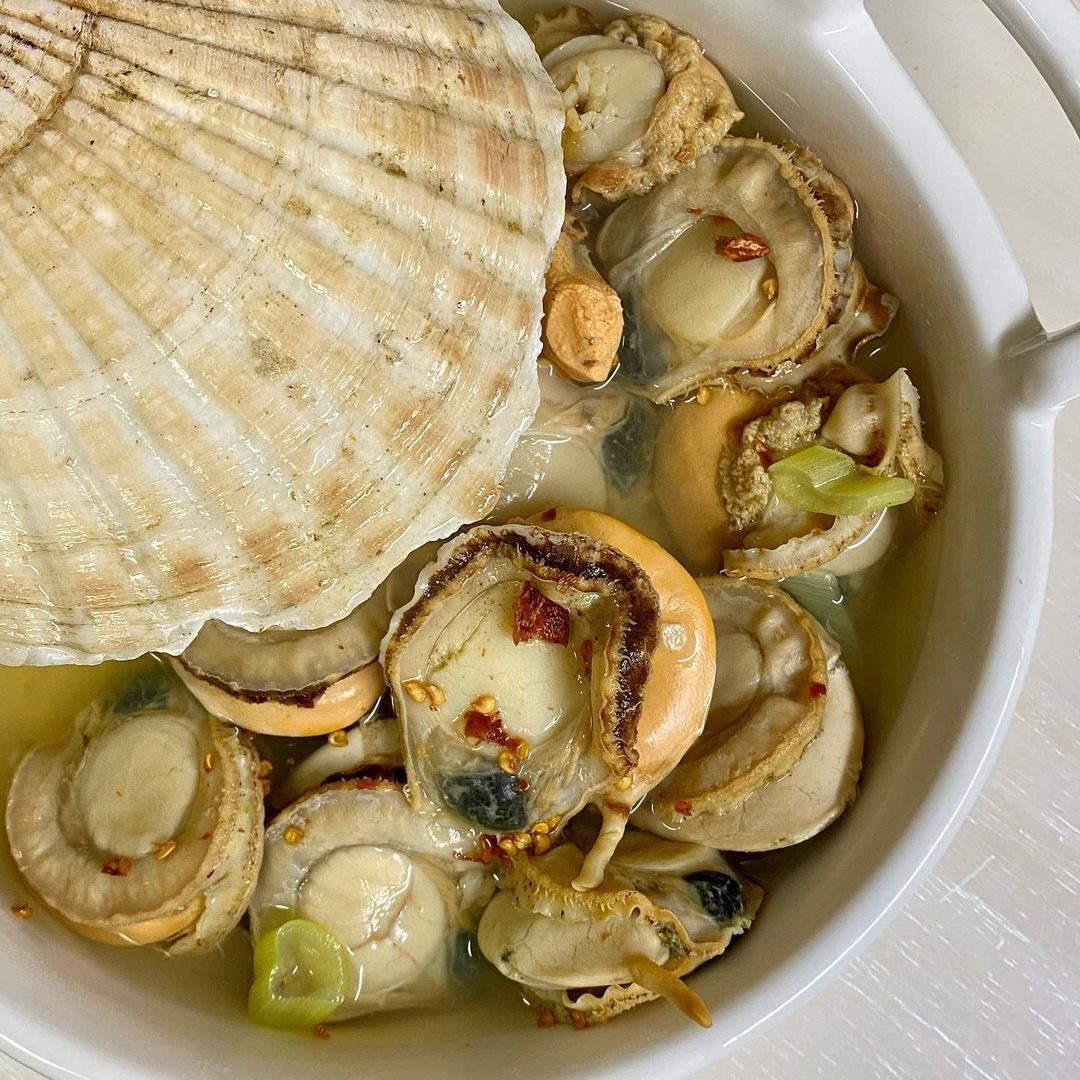 Bowl of clear scallop soup with shellfish, chili peppers, and green onions