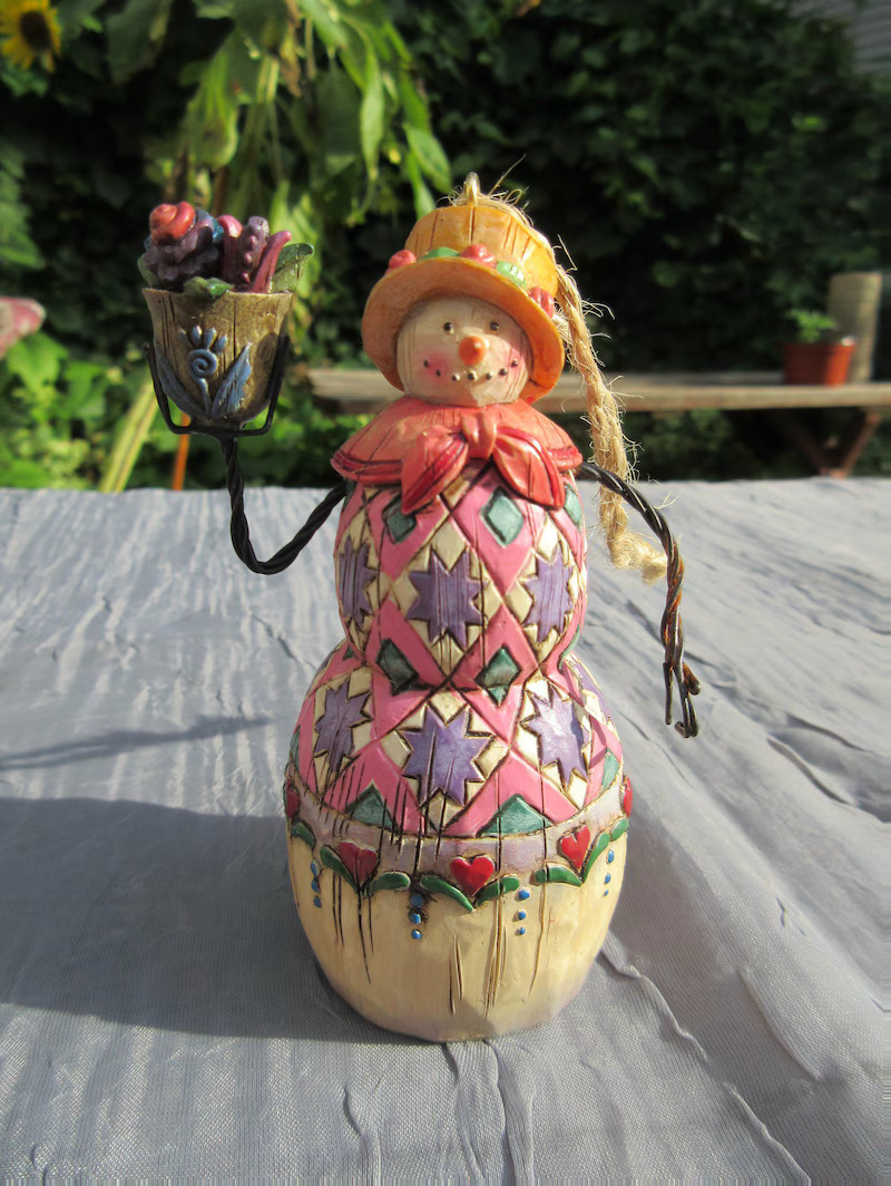 Colorful painted snowman figurine holding lantern on white wooden deck
