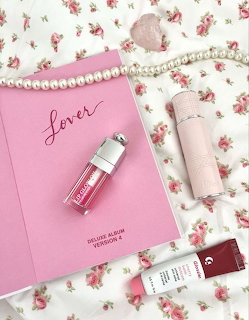 Pink Lover album, lip gloss, pearl necklace, pink tumbler, and rose quartz on a floral bedsheet