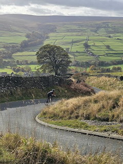 Cyclist on a winding road above Nidderdale valley with green fields and dry stone walls, North Yorkshire