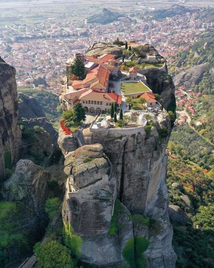 Monastery with red roofs on tall rock formation above Greek town