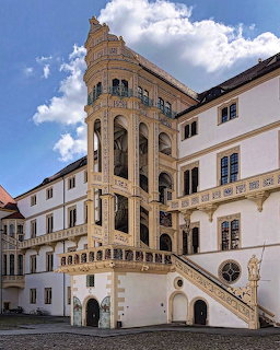 Historic castle courtyard with an ornate tower, arched balconies, and stone staircase