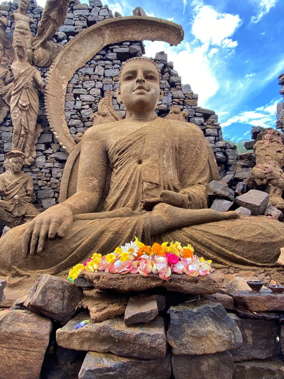 Seated stone Buddha statue with colorful flower offerings at ancient temple ruins in Sri Lanka