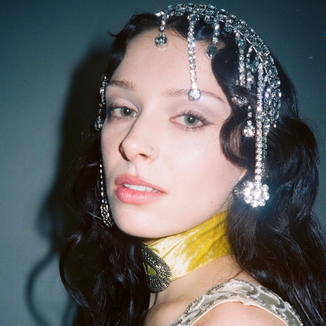 Close-up portrait of Holly Humberstone with a jeweled headpiece and yellow neck accessory