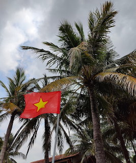 Vietnamese flag flying among palm trees against cloudy blue sky