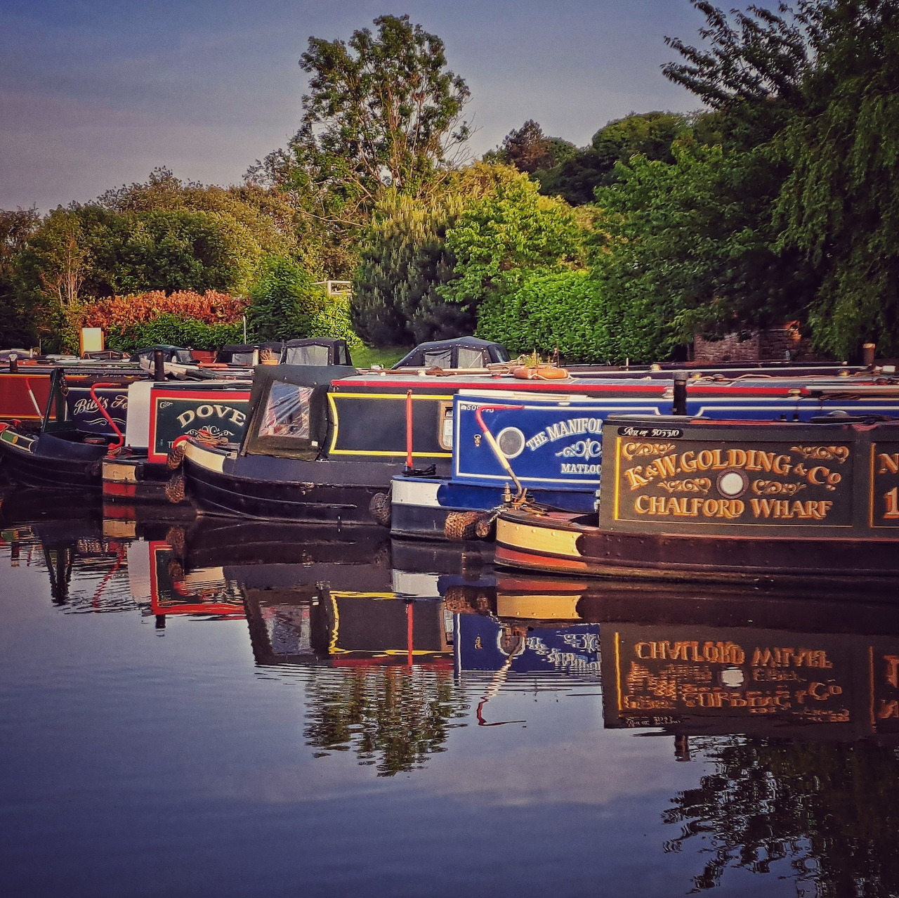 Colorful narrowboats moored on a peaceful canal with tree reflections in calm water