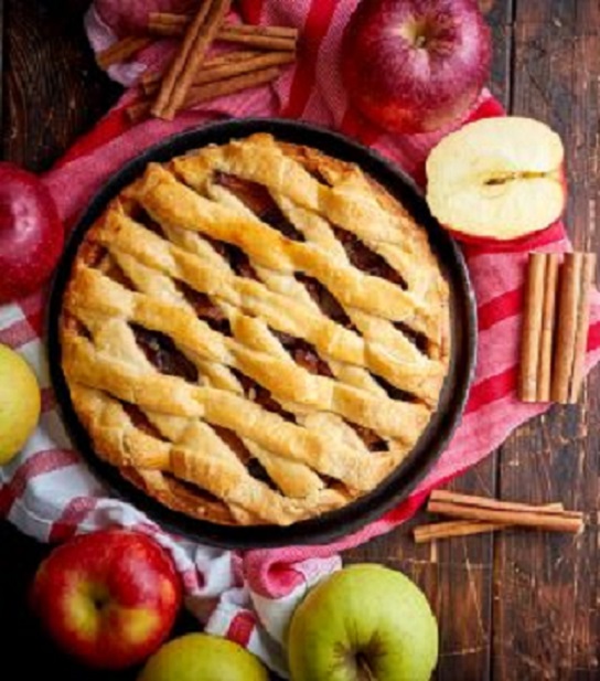 Lattice apple pie in a pan with apples and cinnamon sticks on a rustic wooden table