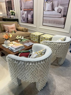 Two white tassel-covered accent chairs in a furnished living room showroom with coffee table and decor