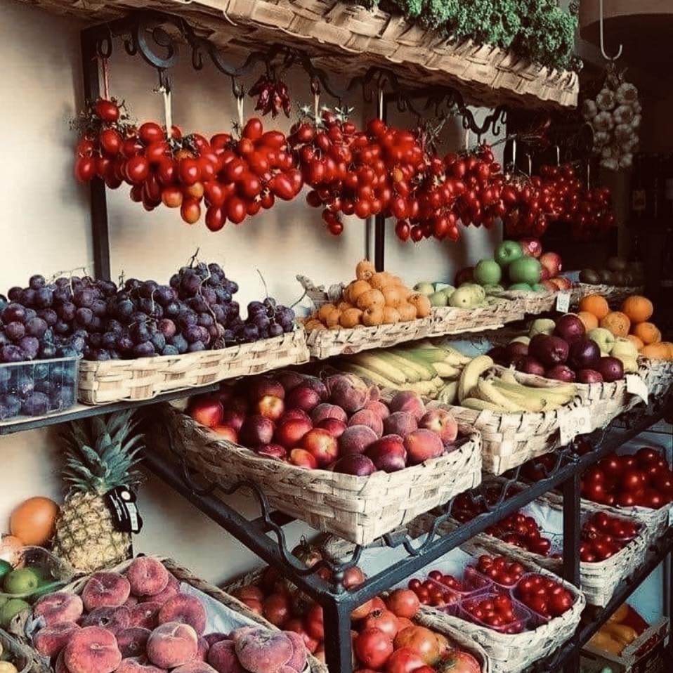 Rustic fruit market stall with baskets of tomatoes, grapes, peaches, bananas, and other fresh produce