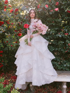 Bride in ruffled white wedding dress holding pink bouquet in a rose garden