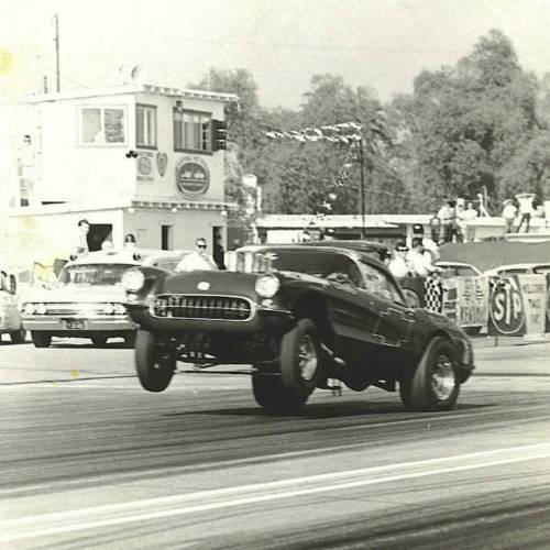 Black vintage Corvette doing a wheelie on a drag strip during a race