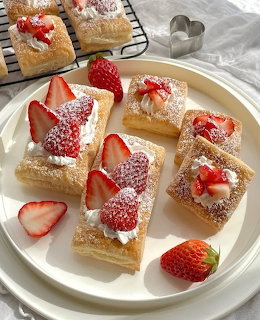 Square pastries with strawberries and cream dusted with powdered sugar on white plate