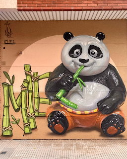 Street art mural showing a cute cartoon panda holding green bamboo stalks against a warm orange wall