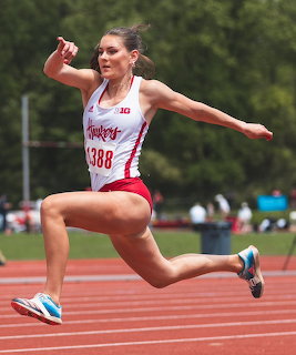 Female athlete in red uniform number 1388 mid-air during a track jump event
