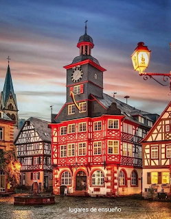 Half-timbered buildings with a clock tower and street lamp at dusk in a European town square