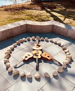 Wooden guitar surrounded by stones in circular pattern on white tiles outdoors